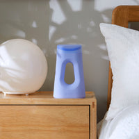 The Loona Personal Bedside Urinal shown in Loona Blue color on a night stand next to a bed in early morning light.